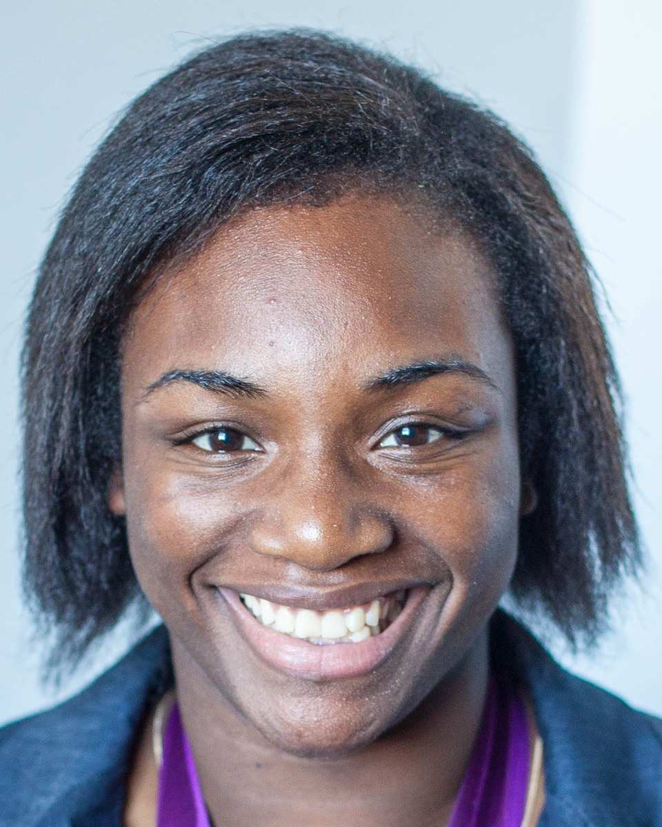 Claressa Shields smiling in a blue blazer, a purple medal ribbon around her neck