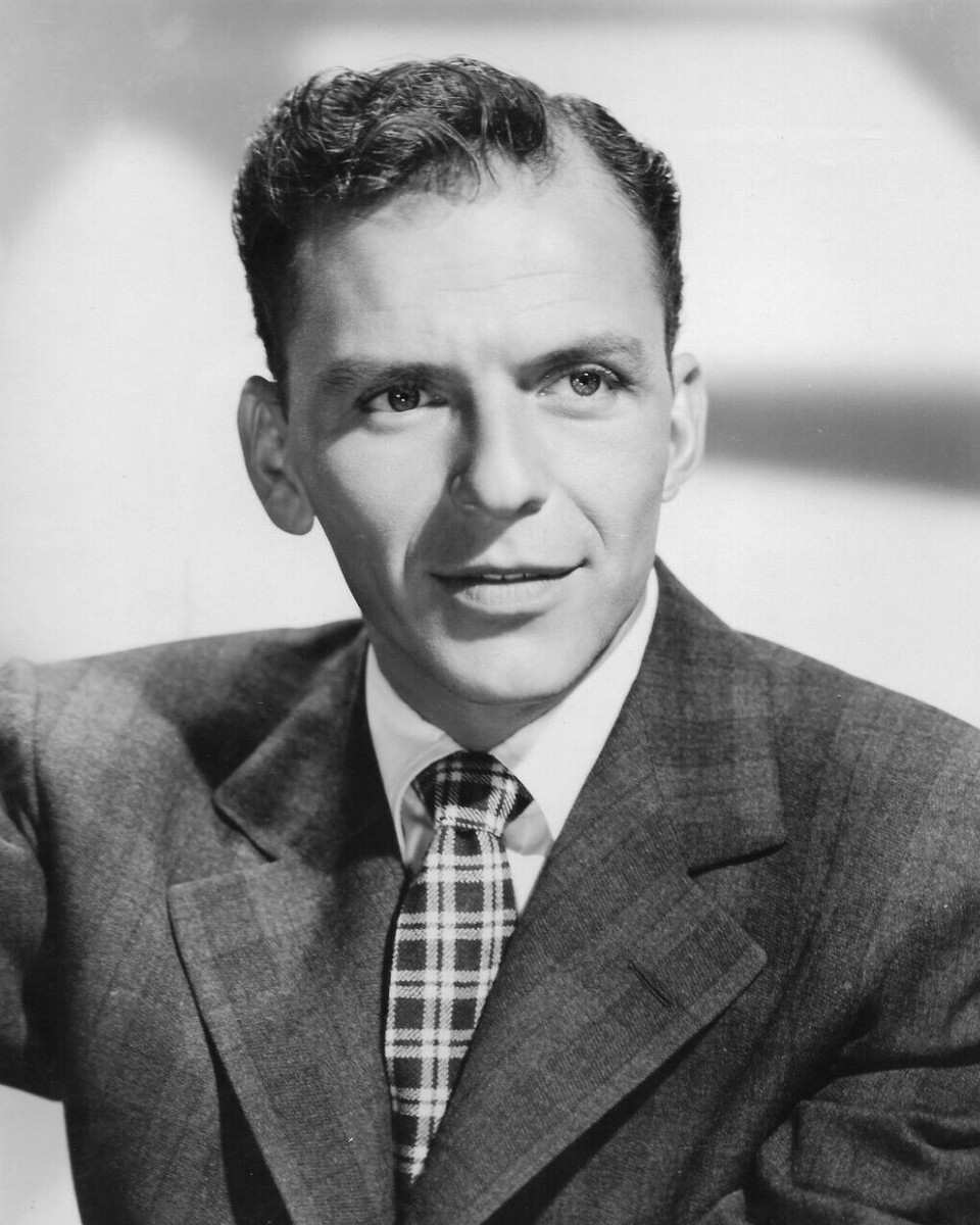 Frank Sinatra in a black-and-white studio portrait, in a textured wool jacket, white shirt and plaid knit tie, with a faint smile