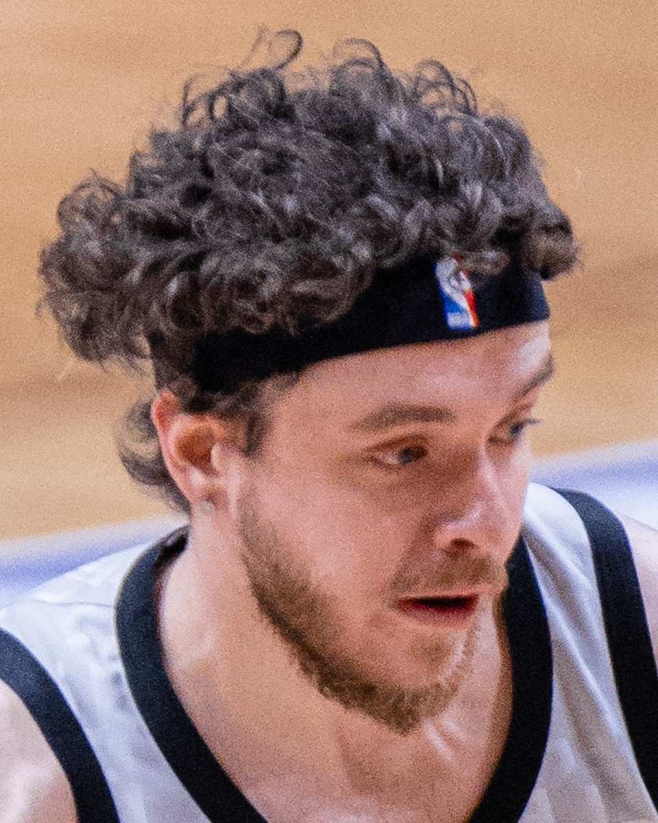 Jack Harlow with curly hair and a black headband, mid-stride on a basketball court