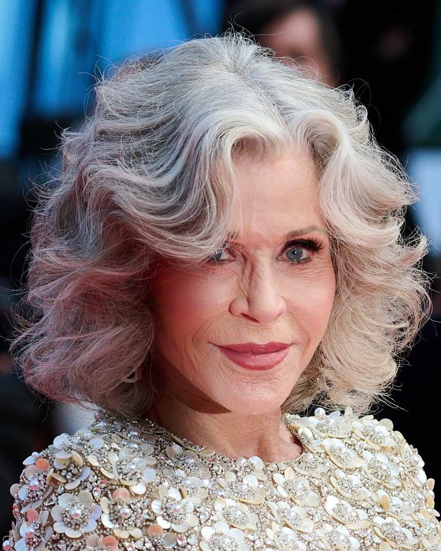 Jane Fonda with wavy silver hair and a faint smile, wearing a cream top covered in beaded floral appliques