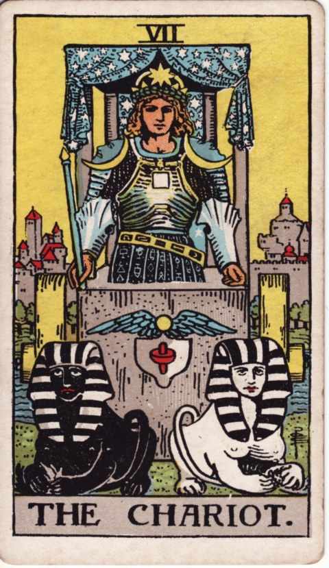 The Chariot card of the Rider–Waite–Smith deck: a man in armor with a starred crown stands in a stone chariot under a starry canopy, a black sphinx and a white sphinx lie in front, a walled town behind