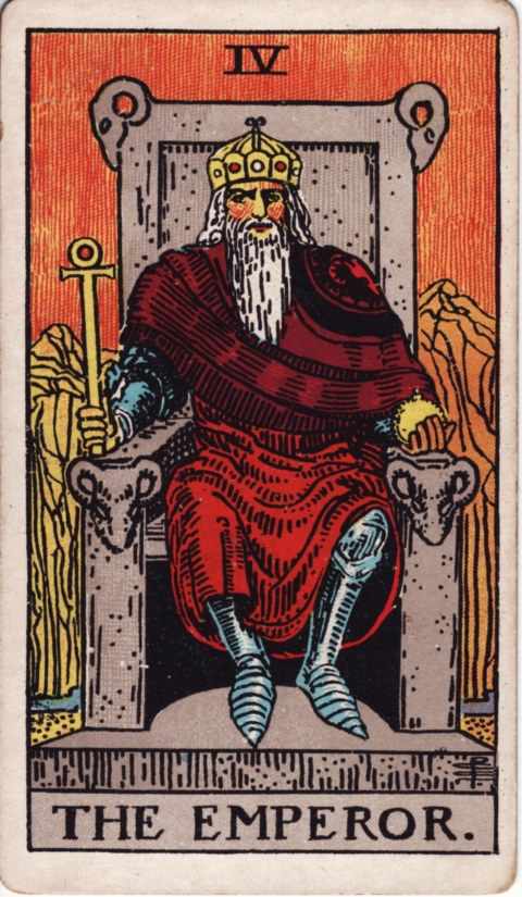 The Emperor card of the Rider–Waite–Smith deck: a white-bearded king in a red robe over armor sits on a stone throne carved with ram heads, holding an ankh scepter and an orb, orange mountains behind