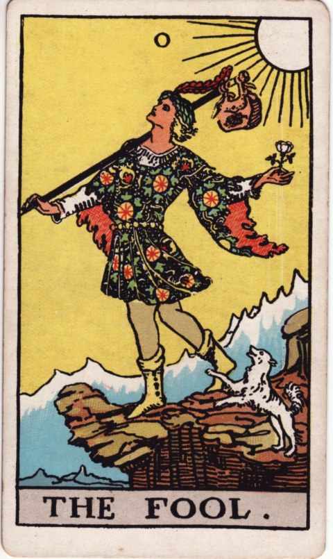 The Fool card of the Rider–Waite–Smith deck: a young man in a bright tunic steps toward a cliff edge holding a white rose, a small white dog leaps at his heels, a white sun and snowy mountains behind
