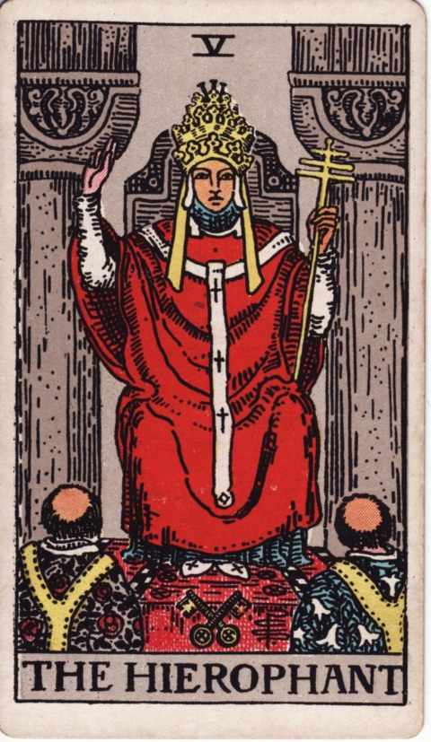 The Hierophant card of the Rider–Waite–Smith deck: a figure in red robes and a triple crown sits between two gray pillars, raising one hand in blessing, two monks kneel before him and two crossed keys lie at his feet