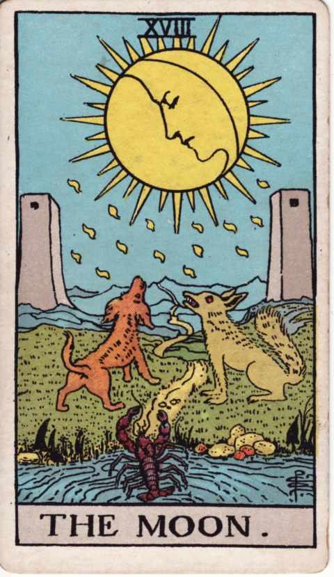 The Moon card of the Rider–Waite–Smith deck: a crescent moon with a sleeping face inside a rayed disc drips yellow drops over a dog and a wolf howling between two gray towers, while a crayfish crawls out of a pool and a path winds toward blue mountains
