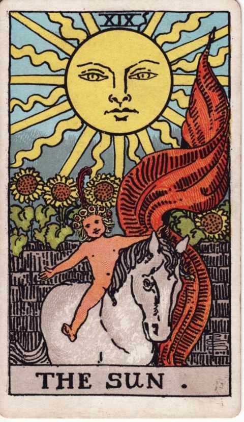 The Sun card of the Rider–Waite–Smith deck: a large smiling sun shines over a gray brick wall with sunflowers, and a naked child in a flower wreath with a red feather rides a white horse, arms wide, beside a flowing red banner